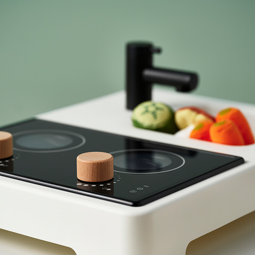 Cocina moderna con estufa negra, perillas de madera, pared verde, grifo negro y verduras picadas.