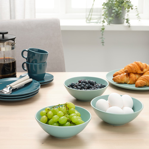 Mesa preparada con tazones de fruta y cruasanes de color azul claro, tazas apiladas y una prensa francesa, lista para el desayuno.