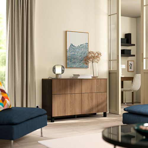 Moderna sala de estar con aparador marrón BESTÅ , libros, flores, lámpara, sofá azul y área de oficina en casa.