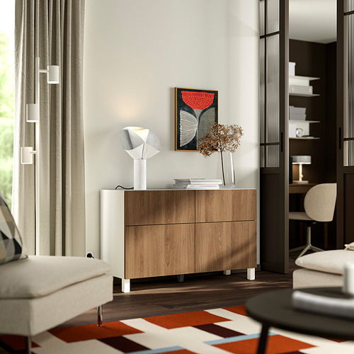 Modern minimalist room with BESTÅ sideboard, lamp, dried flowers, rug, armchair, window, and bookshelf.