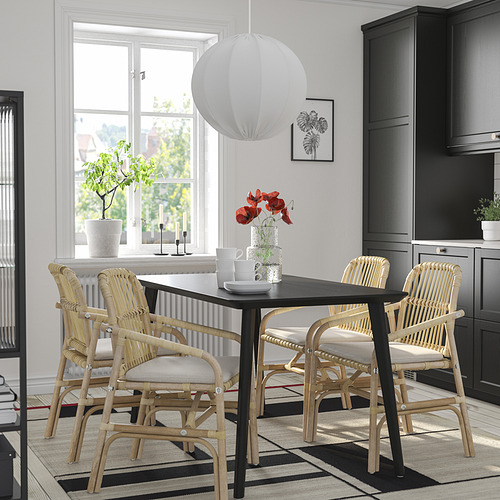 Comedor moderno con mesa negra, cuatro sillas de mimbre, cojines grises. Lámpara colgante blanca, alfombra a rayas, arte de pared. Agradable y acogedor para las comidas.