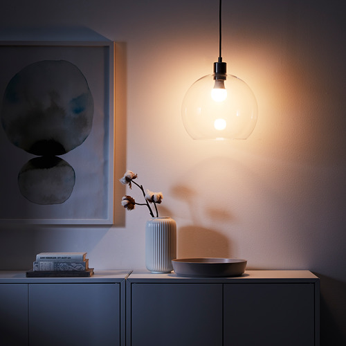 Acogedora habitación con lámpara colgante de vidrio JAKOBSBYN, luz suave, decoración gris, libros y jarrón blanco con rama de algodón.