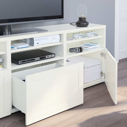 Mueble de TV blanco con puertas de vidrio, donde se guardan consolas de juegos, controladores y auriculares. Sostiene computadora portátil y dispositivos con estantes ajustables.