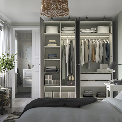Dormitorio moderno con armario abierto que exhibe ropa y artículos doblados. Lámpara colgante sobre la cama; mesa auxiliar con lámpara; plantas y cajas de almacenamiento.