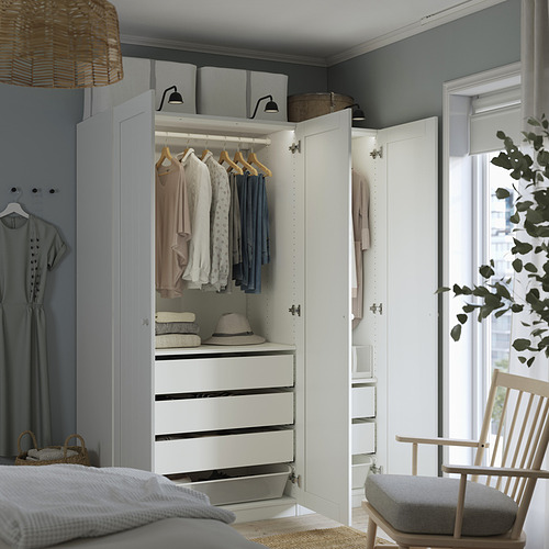 Dormitorio con armario abierto blanco que muestra ropa, cajones y cajas de almacenamiento. Cesta y sombrero en la parte superior, perchas iluminadas.