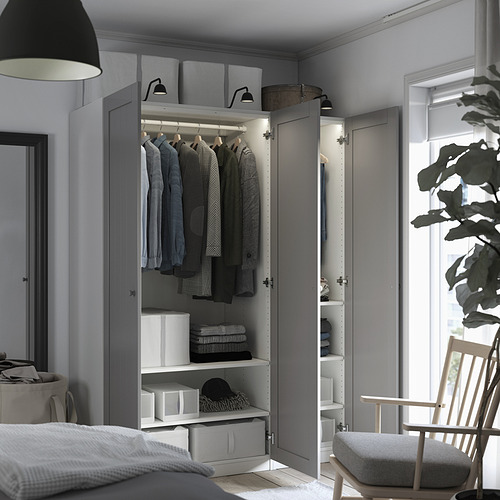 Modern closet with doors open, displaying clothes and shelves. Storage boxes and a chair are visible, withinterior lights illuminating the contents.
