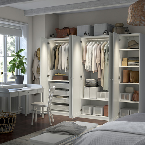 Organized bedroom with white PAX wardrobes. Shelves with white boxes and clothes. Small desk by window.