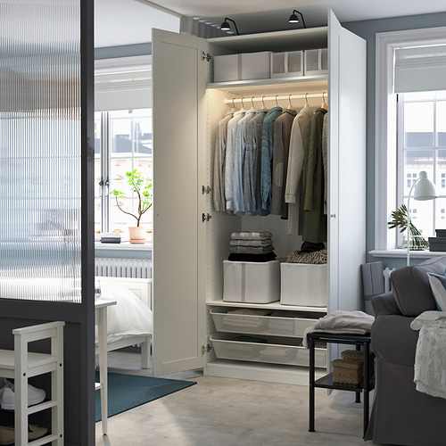 Armario abierto que muestra ropa, artículos doblados y cajas de almacenamiento dentro de una habitación luminosa y organizada.