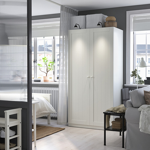 Dormitorio con gran armario blanco, planta en maceta y decoración minimalista.