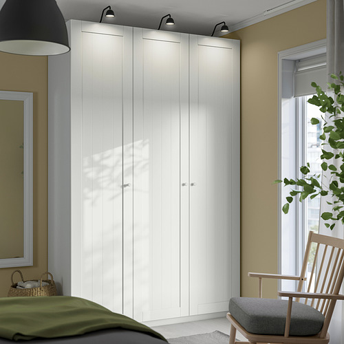 Armario PAX blanco, alto y elegante, junto a la ventana, junto a la mecedora de madera. Diseño alto y minimalista en un dormitorio tranquilo.