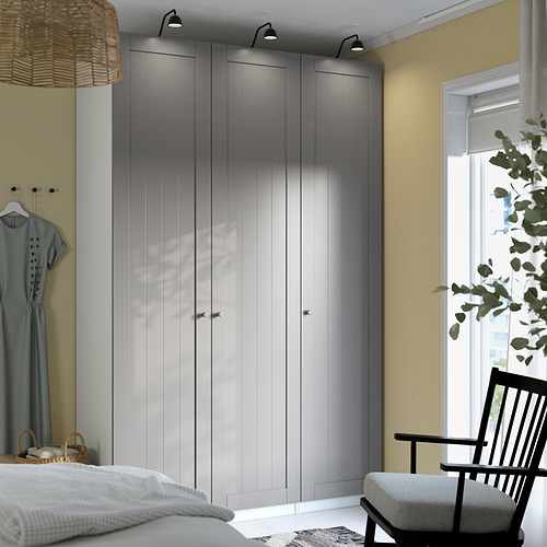 Modern bedroom with large gray PAX wardrobe, sleek design, tall and narrow, with lights and hangers, beside a cozy black chair.