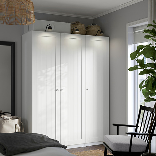 Moderno armario esquinero blanco con cestas de mimbre, ventana, planta, silla acogedora.