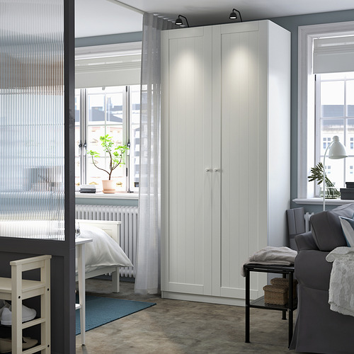 Espacio de trabajo moderno y minimalista con un armario PAX blanco alto y elegante, cortinas grises y asientos acogedores. Diseño limpio y sencillo.
