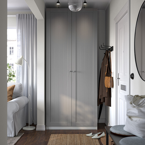 Entrada moderna con un gran armario PAX gris, percheros y un pequeño sillón blanco junto a la ventana. El guardarropa es grande, alto y delgado.