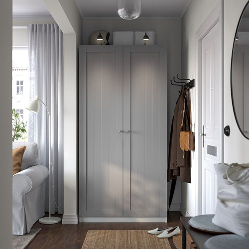 Dormitorio moderno con armario PAX gris, cortinas transparentes, silla, lámpara y espejo.