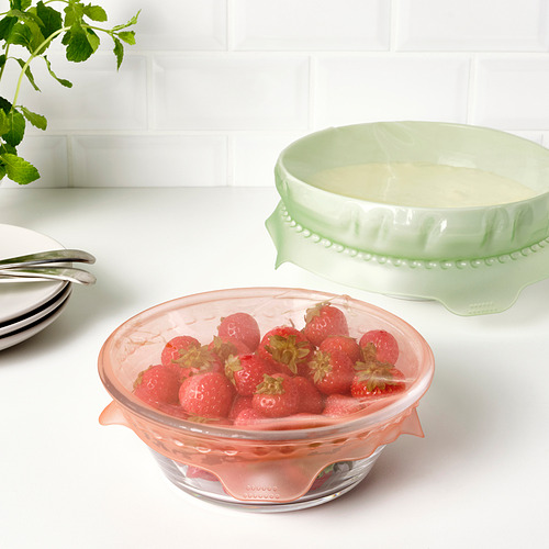Dos cuencos de cristal con tapa: uno con fresas frescas, otro con nata. Los tazones están sobre una encimera blanca.
