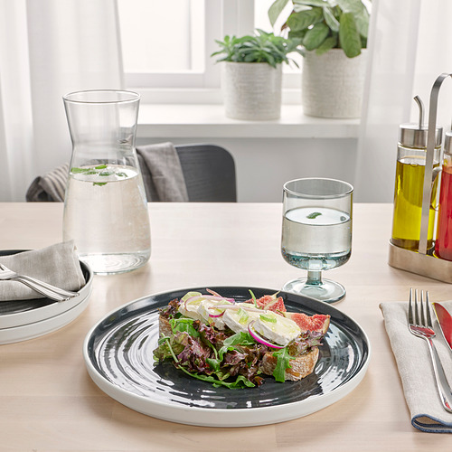 Una mesa rústica con un plato de cerámica que contiene una ensalada y tomates en rodajas. Vasos con agua, una jarra y botellas de aceite se encuentran sobre la mesa.