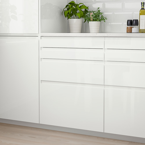 Modernos gabinetes de cocina blancos, elegantes y sin manijas. Tres plantas verdes, botella de vino y copas en la parte superior.
