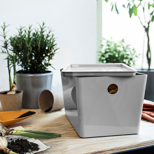 Caja KUGGIS gris claro sobre mesa de madera con plantas. Plástico pet reciclado, diseño rectangular y apilable. Más pequeño que una planta en maceta.