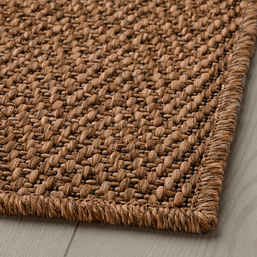 Alfombra de tejido natural, de tejido plano, aspecto rústico, material duradero, sobre suelo de madera.