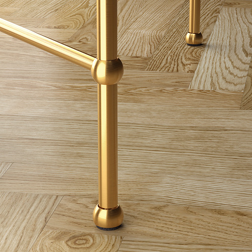 Patas de metal dorado de una mesa con tapa de vidrio, que muestran una elegante artesanía y estabilidad con pies ajustables sobre un piso de madera.