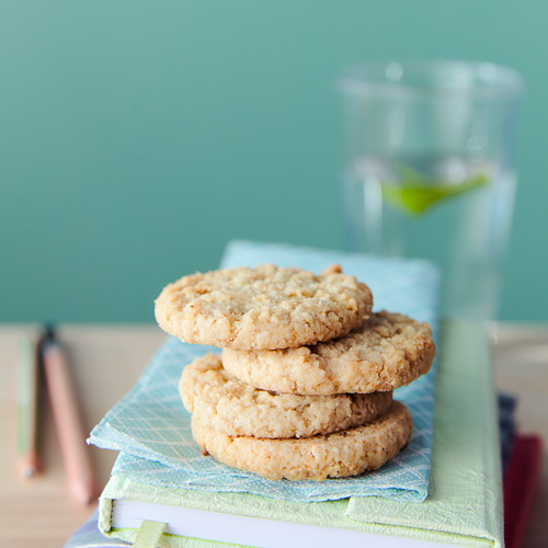 Pila de cuatro galletas de avena en servilleta azul, vidrio, pared verde claro.
