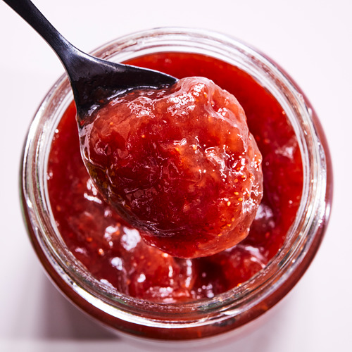 Un frasco de mermelada de fresa de color rojo brillante con una cucharada levantada, frasco de vidrio.