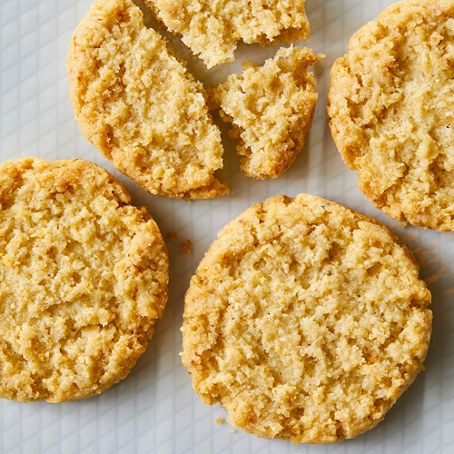 Seis galletas redondas de avena de color marrón dorado sobre una superficie blanca. Uno está roto, mostrando una textura desmenuzable.