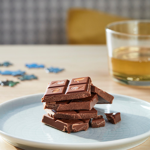 Plato de barras de chocolate negro apiladas junto a un vaso de líquido ámbar.