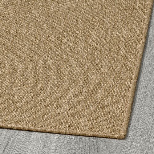 Alfombra de exterior suave de color beige con tejido detallado, expuesta sobre un suelo de madera.