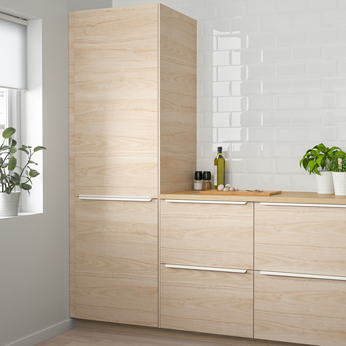 Moderno gabinete de cocina de fresno claro con vetas de madera, manijas elegantes, azulejos blancos y plantas.