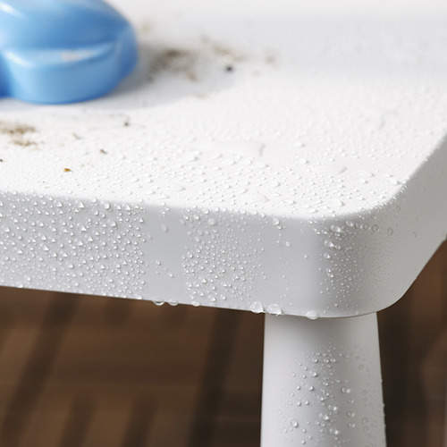 Gotas de agua en el borde blanco de la mesa infantil al aire libre. El artículo azul se encuentra encima de la mesa. Perfecto para picnics.