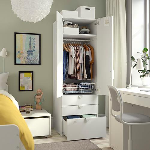 A kids room with a white SMÅSTAD wardrobe displaying various clothes, with open drawers and shelves, positioned near a window with light coming in.