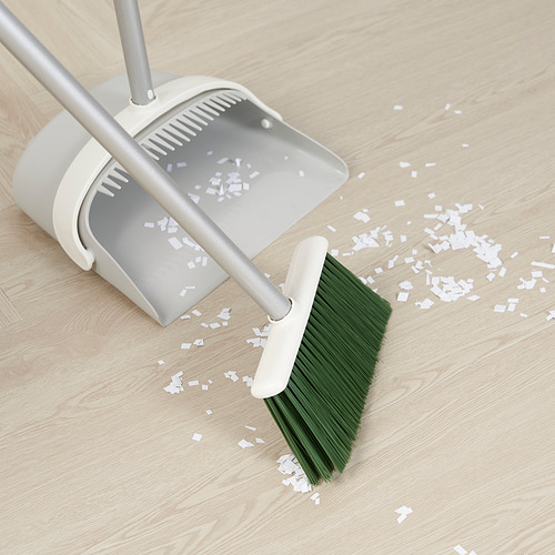Cepillo verde y blanco con recogedor barriendo los escombros del piso de madera.