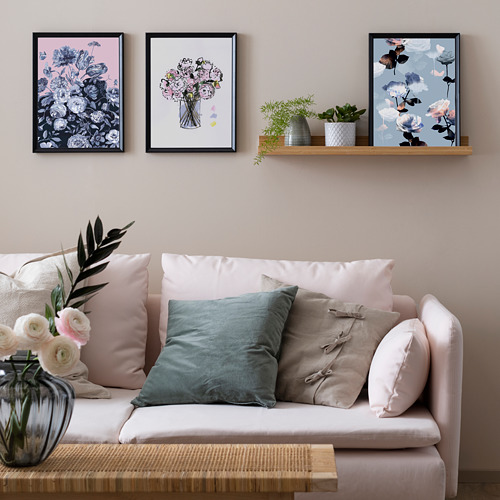 Sala de estar luminosa con arte floral en la pared, un sofá blanco adornado con cojines rosas, azules y beige y plantas en macetas en un estante de madera.