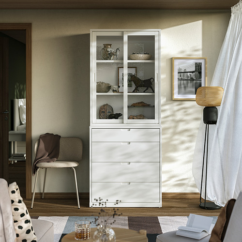 Sala de estar moderna con mueble y silla TONSTAD blancos, elementos decorativos, libros, lámpara y cortina de ventana.