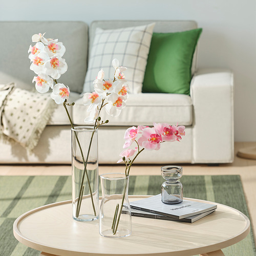 Sala de estar moderna con sofá blanco, almohadas de colores, mesa de café con libros, velas y orquídeas.