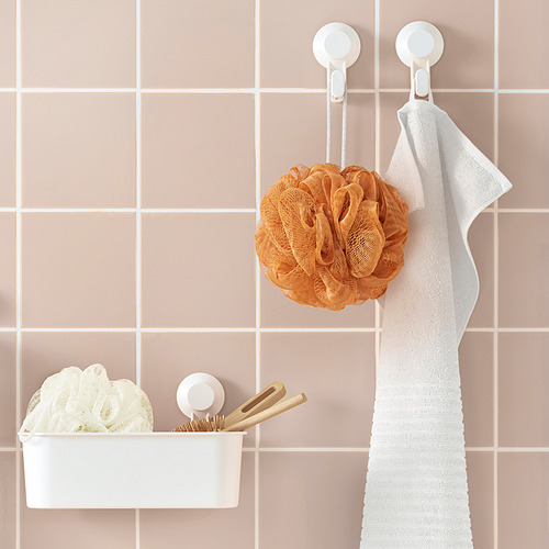 Almacenamiento simple en el baño: cesta blanca, puff de cuerpo naranja, toalla para colgar en azulejos de pared rosas.