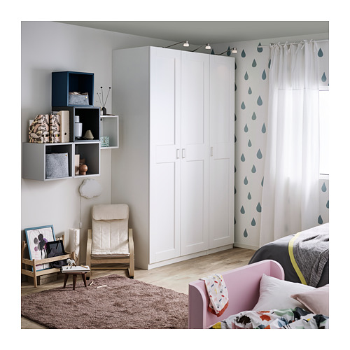 Dormitorio moderno con armario GRIMO blanco, cama rosa, almohadas de colores, silla de madera, alfombra y estantes de pared.