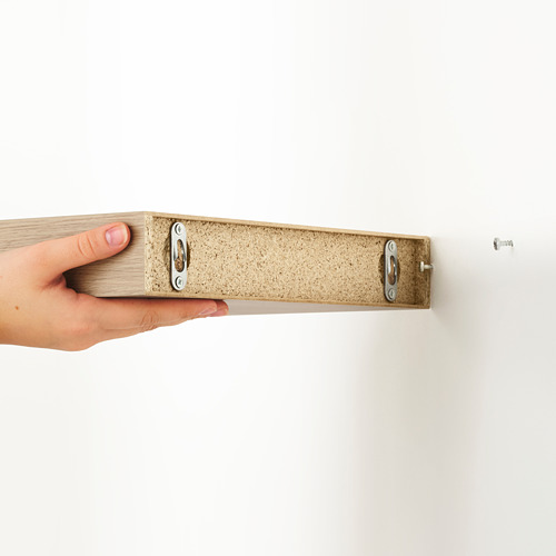 Estante de pared LACK sosteniendo con la mano por el borde, mostrando soportes de montaje ocultos y diseño minimalista.