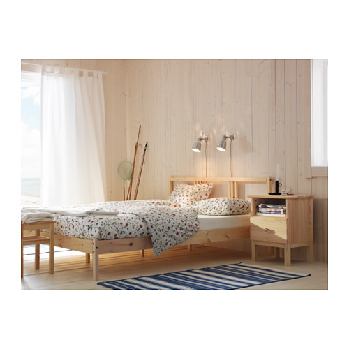 Dormitorio con cama y cajón de madera clara TARVA; lecho floral; lámparas de pared; Alfombra de rayas, sencillo diseño escandinavo.