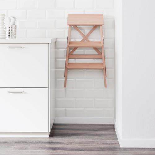 Taburete plegable de madera junto a armarios blancos.