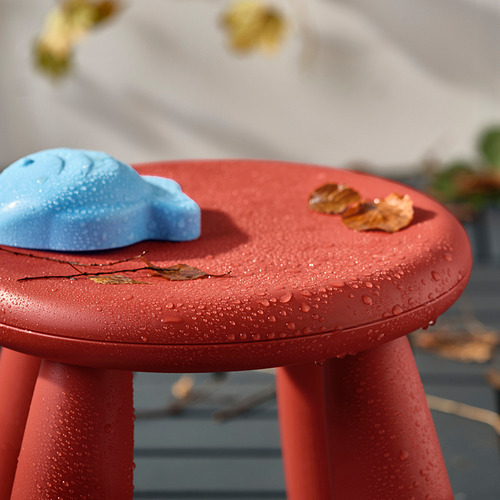 Taburete infantil rojo con juguete azul y hojas, al aire libre