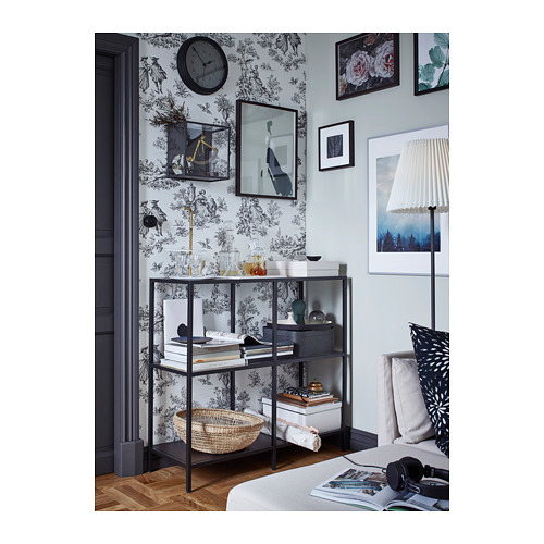 Dormitorio floral con estantería VITTSJÖ, jarrones, libros, reloj, lámpara, cojines.