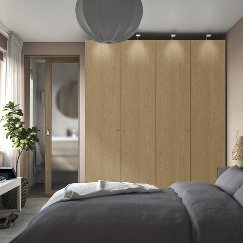 Dormitorio moderno con armario PAX, cama y planta. Armario dominante, madera clara, iluminación sutil.