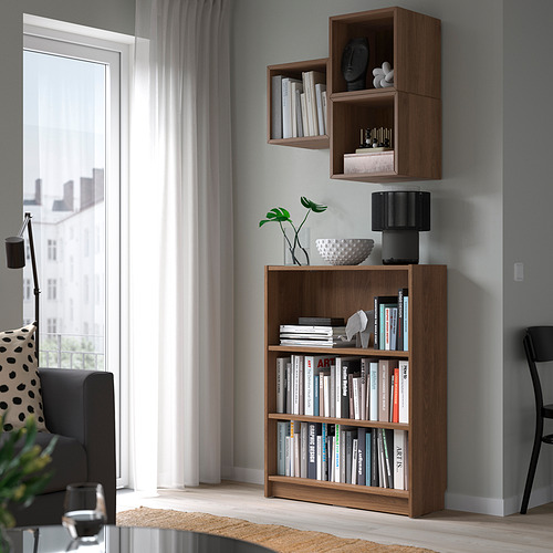 Estantería de madera con libros, lámpara, planta, junto a la ventana. Pared gris, dos estantes superiores.