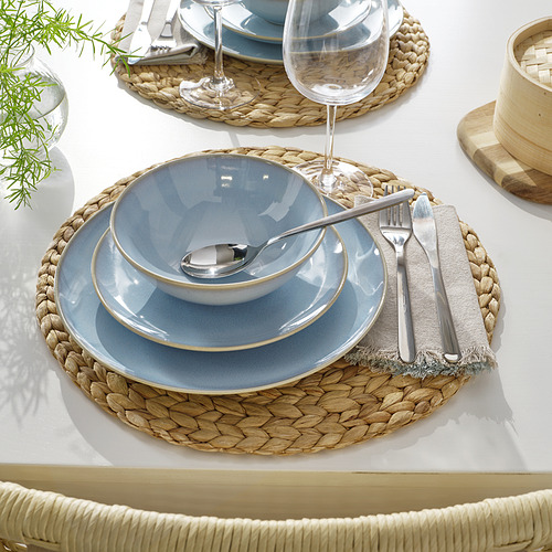 Configuración de la cena con platos azules, tazones, cubiertos y manteles individuales tejidos.