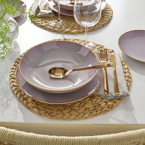 Elegante vajilla con platos morados, cubiertos dorados y mantel individual tejido sobre una mesa blanca. Perfecto para comidas elegantes.