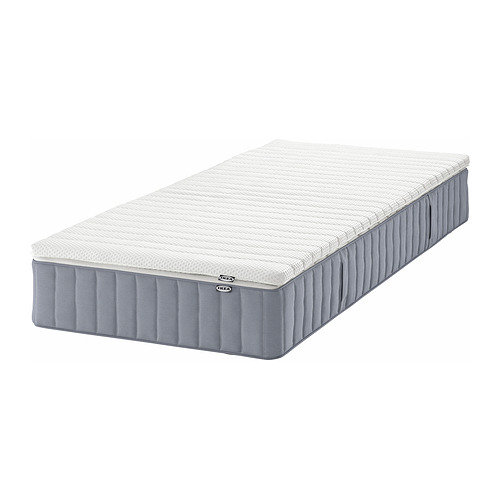 Un colchón de muelles ensacados VALEVÅG de IKEA con una funda gris claro y una capa superior blanca, diseñado para una sensación más firme, enrollado para facilitar el transporte.