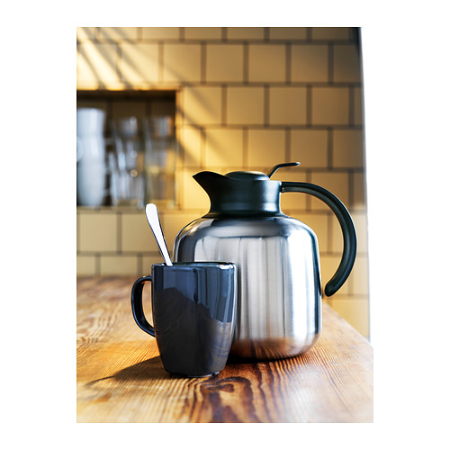 Un elegante matraz de vacío negro SLUKA con asa se encuentra sobre una mesa de madera junto a una taza negra a juego.